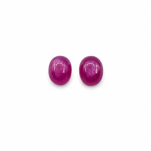 May include: Two oval-shaped, cabochon-cut gemstones with a deep magenta-pink color. Each stone features a smooth, polished, and rounded surface that reflects light, showcasing a consistent, vibrant, and saturated hue across the entire surface.
