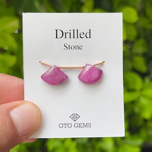 May include: Two pink drilled stones on a white card with the text "Drilled Stone" and "GTCG GEMS".