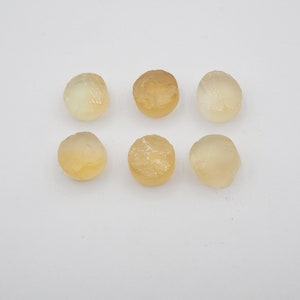 May include: Seven round, translucent, yellow-toned gemstones with a rough, textured surface.