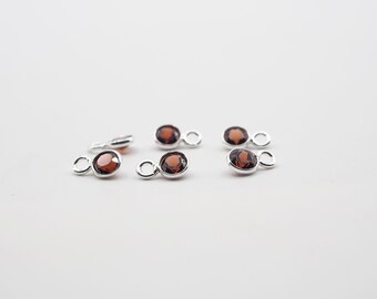 May include: Five silver charms with a small round red gemstone in the center. Each charm has a small loop on the top for attaching to a bracelet or necklace.