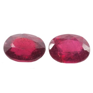 May include: Two oval-shaped, red gemstones with a faceted cut.