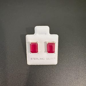 May include: A pair of rectangular red gemstone stud earrings set in sterling silver, mounted on a white display card with the text STERLING SILVER printed in black at the bottom center of the card.