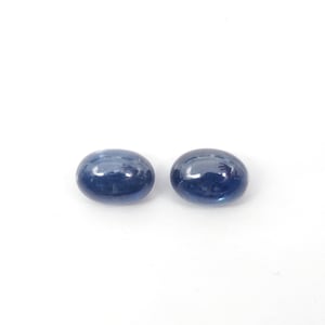 May include: Two oval-shaped blue gemstones, likely sapphires, on a white background.
