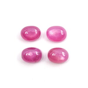 May include: Four oval-shaped, polished gemstones in a vibrant pink hue are arranged on a white surface. The gems have a smooth, rounded appearance, reflecting light and showcasing their color. These gemstones are ideal for jewelry making.