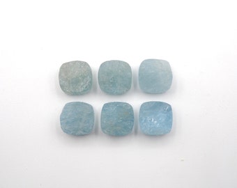May include: Six light blue aquamarine gemstone cabochons, each with a square shape and a slightly irregular, textured surface.