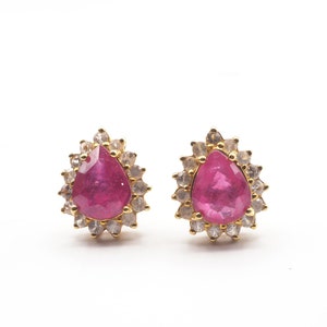 May include: A pair of gold earrings with a teardrop-shaped pink gemstone surrounded by smaller white gemstones.