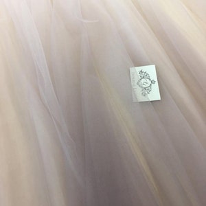 Könnte beinhalten: Eine Nahaufnahme eines durchsichtigen, weißen Tüllstoffes. Der Stoff ist weich und zart, mit einem dezenten Glanz. Der Stoff ist perfekt für die Herstellung einer Vielzahl von Kleidungsstücken, wie Kleider, Röcke und Schleier.
