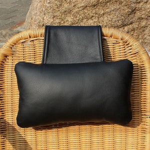Könnte beinhalten: Schwarzes Leder-Kopfstützenkissen für einen Korbstuhl. Das Kissen ist rechteckig und hat ein schlichtes Design.