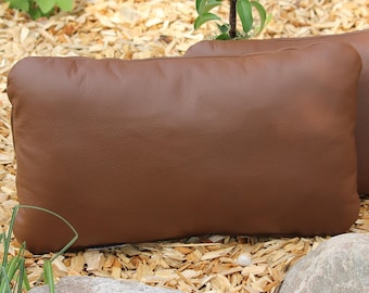 May include: Two brown leather throw pillows on a bed of wood chips.