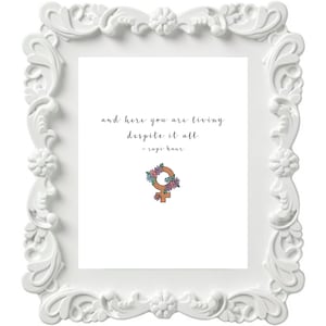 Peut inclure: Cadre blanc orné avec une citation à l'intérieur : "and here you are living despite it all - rupi kaur". Un symbole féminin brun avec des fleurs roses et violettes autour est au centre du cadre.