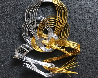 May include: A silver and gold decorative knot made of wire. The knot is tied in a complex pattern and has a three-dimensional shape.
