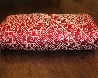 Puede incluir: Un cojín rojo y blanco con un diseño geométrico. El cojín es rectangular y tiene una textura suave y mullida.