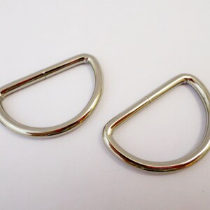 Könnte beinhalten: Zwei silberne D-Ringe aus Metall. Die Ringe sind glatt und glänzend.