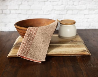 May include: A wooden bowl, a beige kitchen towel with red stripes, and a white ceramic jar with a wooden lid on a brown wooden table.