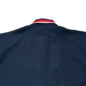 K&ouml;nnte beinhalten: Marineblaues Hemd mit rot-wei&szlig; gestreiftem Kragen. Das Hemd hat eine Tasche auf der unteren R&uuml;ckseite. Der Kragen hat ein klassisches Design, und das Hemd scheint aus einem glatten Stoff zu sein.
