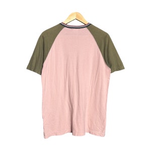 May include: A pink and green short-sleeved t-shirt with a contrasting color design. The shirt has a crew neck and a striped trim around the neck.