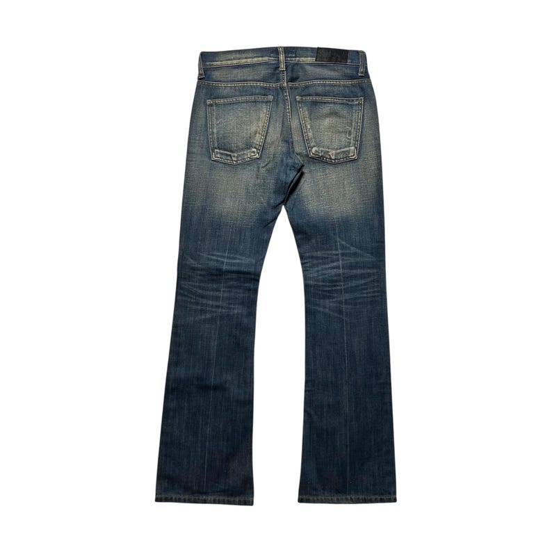 May include: Back view of blue denim jeans with a faded wash. The jeans have a classic five-pocket design, belt loops, and a button and zipper closure. The denim has subtle distressing and fading, giving it a worn-in look. The jeans have a slight bootcut leg opening.