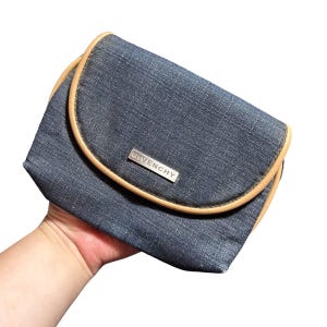 May include: A small, dark blue denim makeup bag with a tan leather trim and a silver metal logo that reads "Givenchy".
