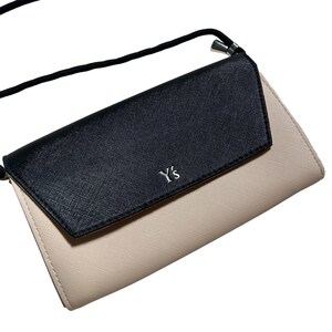 May include: A black and beige leather clutch bag with a shoulder strap and the logo "Y's" on the front.