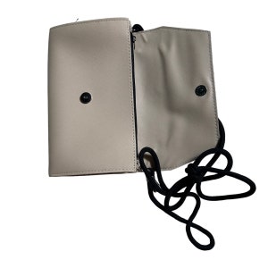 May include: A beige leather crossbody bag with a black adjustable strap. The bag has a flap closure and a zippered pocket on the front.
