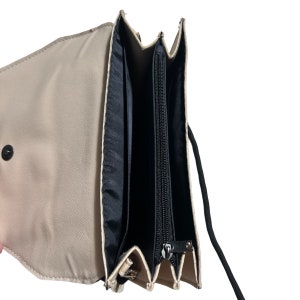 May include: A beige leather crossbody bag with a black zipper closure and a black strap. The bag is open and the inside is lined with black fabric.