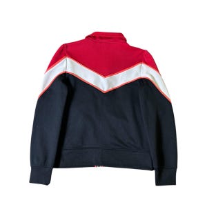 K&ouml;nnte beinhalten: Eine schwarze, rote und wei&szlig;e Jacke mit Rei&szlig;verschluss. Die Jacke hat einen roten Kragen und ein Zickzack-Design auf der Brust in Rot, Wei&szlig; und Orange. Die &Auml;rmel und der untere Teil der Jacke sind schwarz.