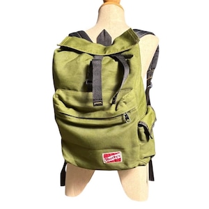 May include: An olive green backpack with black straps and a front pocket. The backpack has a flap closure and a side pocket. The brand name "Shorty's" is displayed on a red and white patch.
