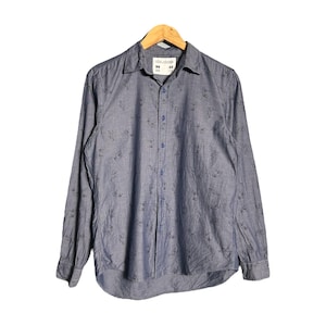 Puede incluir: Una camisa azul de manga larga con botones y un pequeño estampado por todas partes. La camisa tiene un cuello puntiagudo y un cierre de botones en la parte delantera. La etiqueta de la camisa dice "35 02".