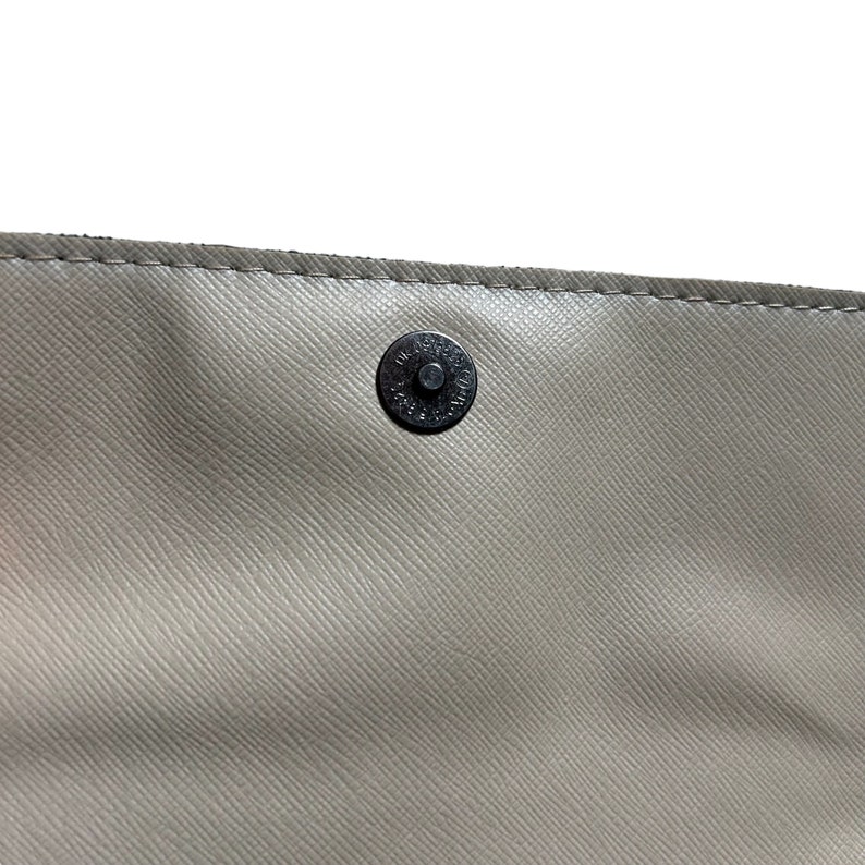 May include: Close-up of a light gray leather purse with a black metal snap closure.
