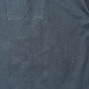 K&ouml;nnte beinhalten: Nahaufnahme eines dunkelblauen Stoffes mit einer sichtbaren Tasche auf der oberen linken Seite. Der Stoff hat ein leicht strukturiertes Aussehen mit subtilen Farb- und Tonvariationen. Die Tasche ist rechteckig und auf den Stoff gen&auml;ht.