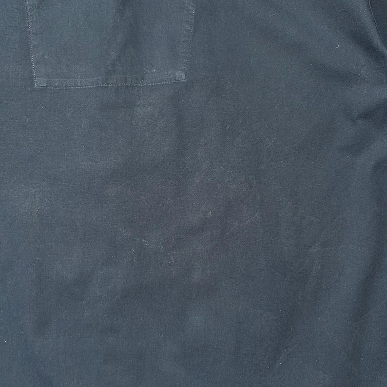 K&ouml;nnte beinhalten: Nahaufnahme eines dunkelblauen Stoffes mit einer sichtbaren Tasche auf der oberen linken Seite. Der Stoff hat ein leicht strukturiertes Aussehen mit subtilen Farb- und Tonvariationen. Die Tasche ist rechteckig und auf den Stoff gen&auml;ht.