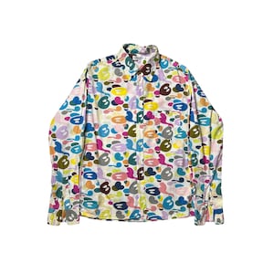 May include: A long-sleeved button-down shirt with a colorful abstract pattern. The shirt features a white base with a repeating design of blue, yellow, pink, and brown shapes. It has a chest pocket and a classic collar.