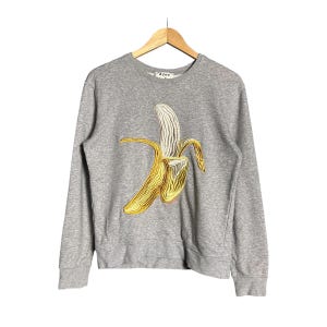 May include: A gray sweatshirt with a yellow banana embroidered on the front. The banana is stylized and has a gold outline. The brand name "Acne" is printed on the tag.