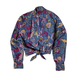 May include: A long-sleeved button-down shirt featuring a vibrant blue base with a multi-colored paisley and floral pattern in shades of magenta, yellow, and green. The shirt has a pointed collar and a front hem that ties into a knot at the waist.