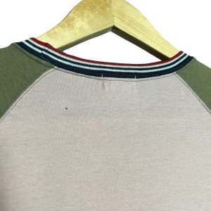 May include: A pink and green raglan t-shirt with a striped navy, white, and red collar.