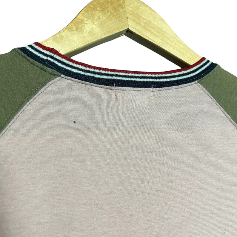 May include: A pink and green raglan t-shirt with a striped navy, white, and red collar.