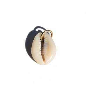 May include: A white cowrie shell with a gold-colored metal loop attached to the top. The shell is a popular charm for jewelry and is often used in spiritual practices.