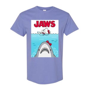 May include: A light purple t-shirt featuring a parody of the movie "Jaws." The graphic shows a cartoon shark with a red bow tie and a cartoon character in the water. The word "JAWS" is printed in red at the top.