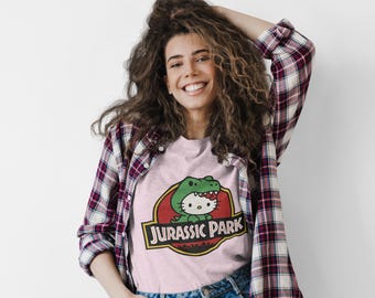 Hello Kitty Jurassic Park T-Shirt | Kawaii Dinosaurier Mashup Tee | Niedliches rosafarbenes grafisches Shirt | Unisex Baumwoll T-Shirt | Lustiges Film Crossover Geschenk