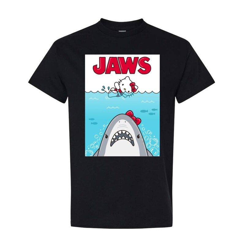 May include: Black t-shirt featuring a parody design. The graphic depicts a shark with a red bow and a cartoon character in the water, with the word "JAWS" in red block letters above. The design is a humorous take on the classic movie poster.