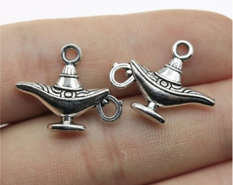 Puede incluir: Dos colgantes de metal plateado con forma de lámpara de genio. Cada colgante tiene un diseño detallado, que incluye una boquilla, un asa y un patrón decorativo. Los colgantes son pequeños, con un lazo en la parte superior para sujetarlos a joyas u otras manualidades.