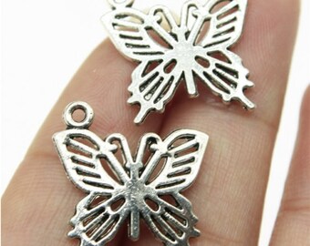 Pode incluir: Dois pingentes de metal prateados em forma de borboleta com designs intrincados recortados. Os pingentes têm um laço na parte superior para serem presos a joias ou outros artesanatos.