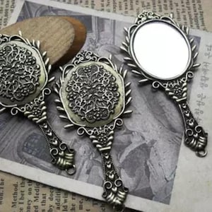 Può includere: Tre specchietti da mano in stile antico decorati con intricati motivi floreali. Gli specchi hanno una finitura argentata e sono perfetti per aggiungere un tocco di fascino vintage a qualsiasi arredamento.