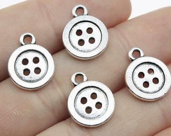 May include: Four circular silver-toned metal charms shaped like buttons, each featuring a raised outer rim and four small holes in the center. Each charm includes a small jump ring at the top for attachment, with a weathered, antique finish.