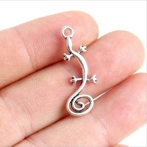 Puede incluir: Encanto de metal plateado en forma de lagarto enroscado con un bucle en la parte superior para sujetarlo a joyas.