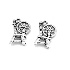 May include: Two silver spinning wheel charms with a loop for hanging. The charms are detailed with a wheel, spindle, and base.