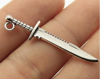 May include: A silver-toned metal sword charm featuring a textured handle, a straight crossguard, and a blade with a serrated spine. The charm includes a small circular loop at the pommel end for attachment to jewelry or other craft projects.