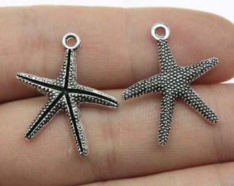 Op de afbeelding: Twee zilverkleurige zeester-bedels met een getextureerd oppervlak. De bedels hebben een lus aan de bovenkant om aan sieraden of andere knutselwerkjes te bevestigen.