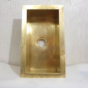 May include: A gold-colored rectangular kitchen sink with a drain hole in the center. The sink is made of metal and has a smooth, polished finish.