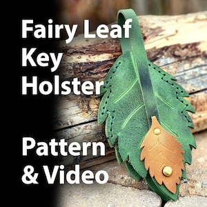 May include: A green leather key holder shaped like a leaf with a smaller brown leaf detail. The key holder has stitching around the edges and a loop at the top for hanging. The text "Fairy Leaf Key Holster Pattern & Video" is visible in the image.